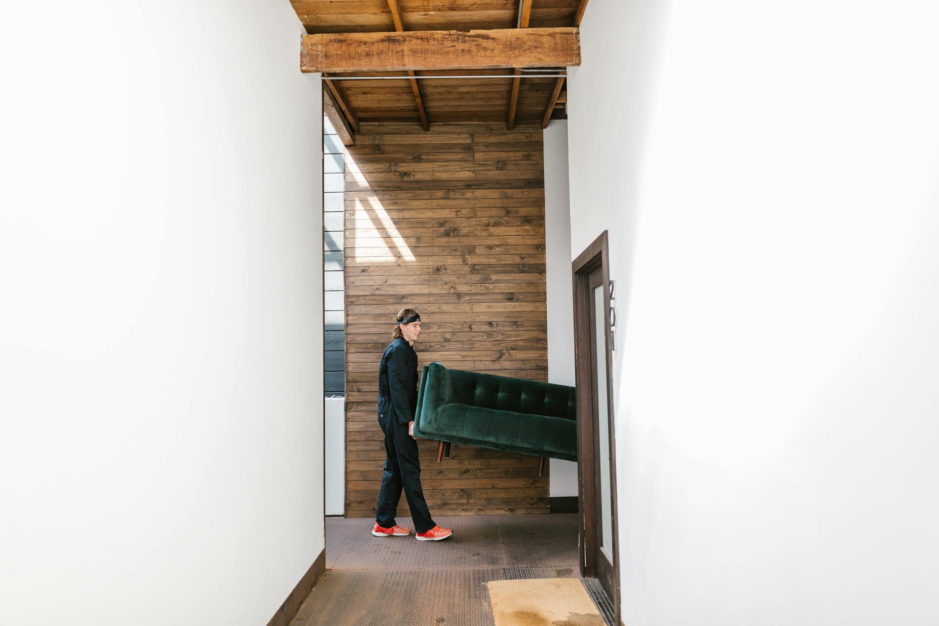 A mover carries a green sofa through a modern wooden hallway, showcasing relocation and moving service.