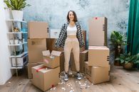 Photo of a Woman in a White Crop Top Standing Beside Cardboard Boxes
