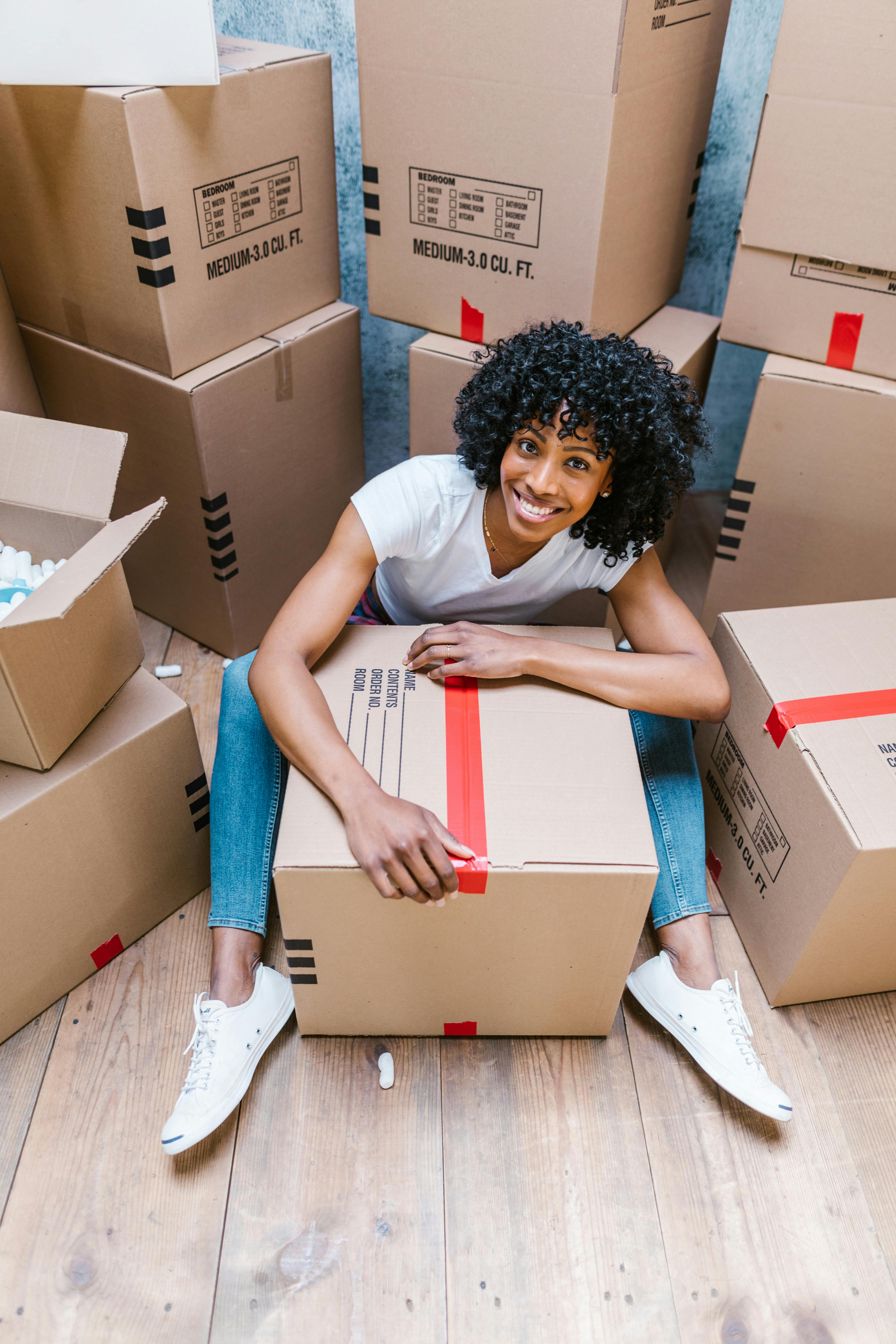 woman in white t shirt and blue denim jeans sitting on brown cardboard box