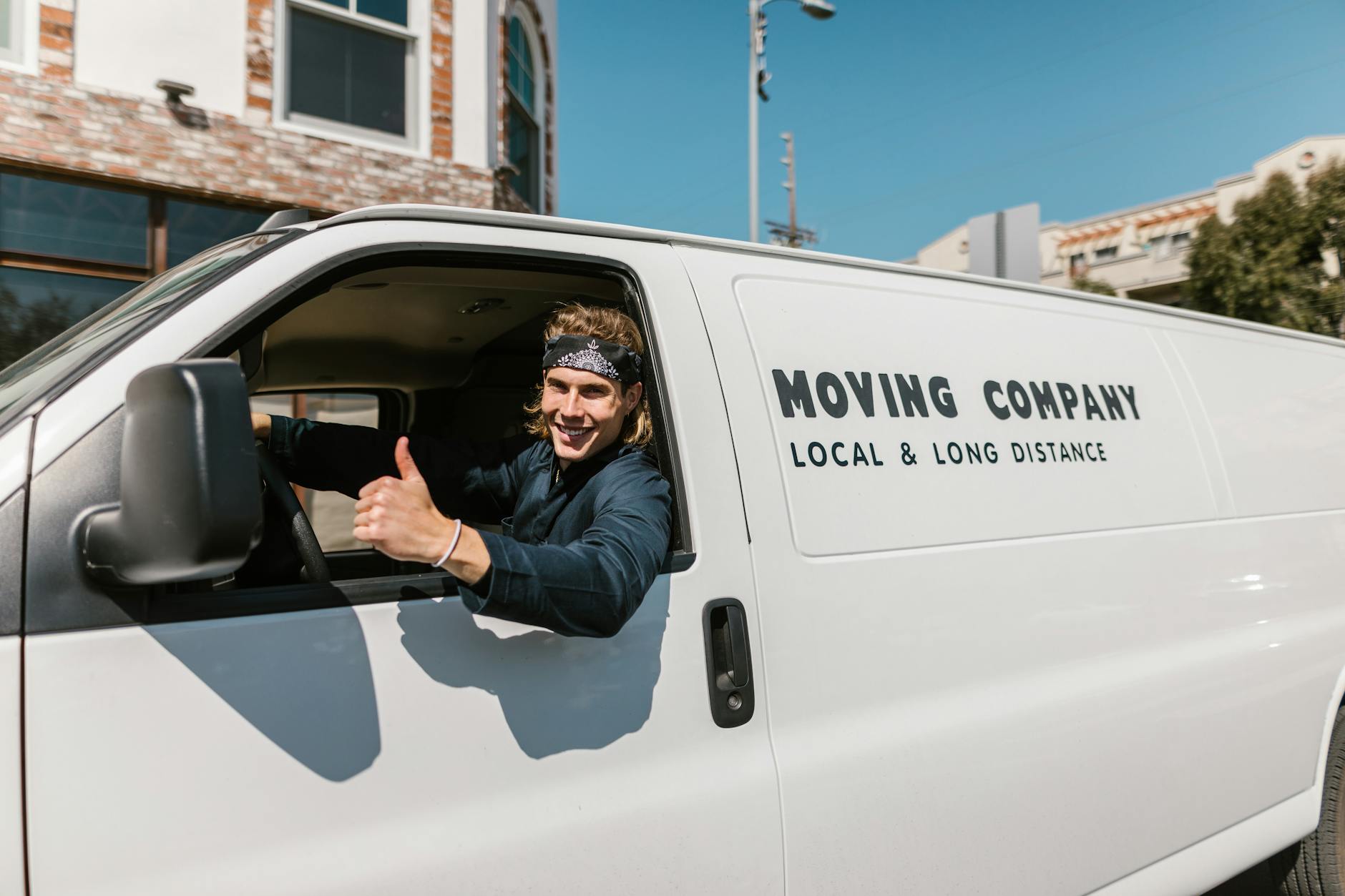 Smiling mover giving thumbs up from a moving company van parked outside. Smiling mover giving thumbs up from a moving company van parked outside.