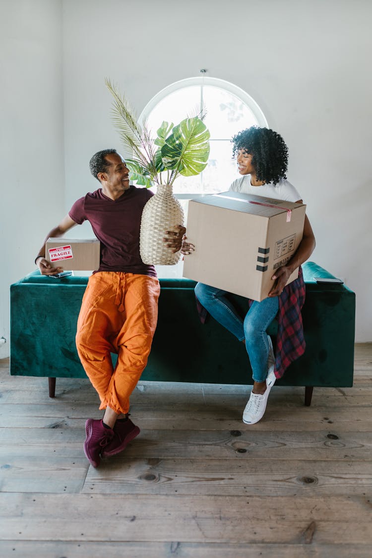 A Couple Carrying Moving Boxes While Sitting On A Couch