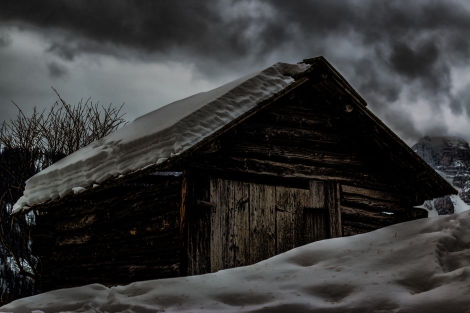 Mysterious rustic cabin blanketed in snow under a moody winter sky.