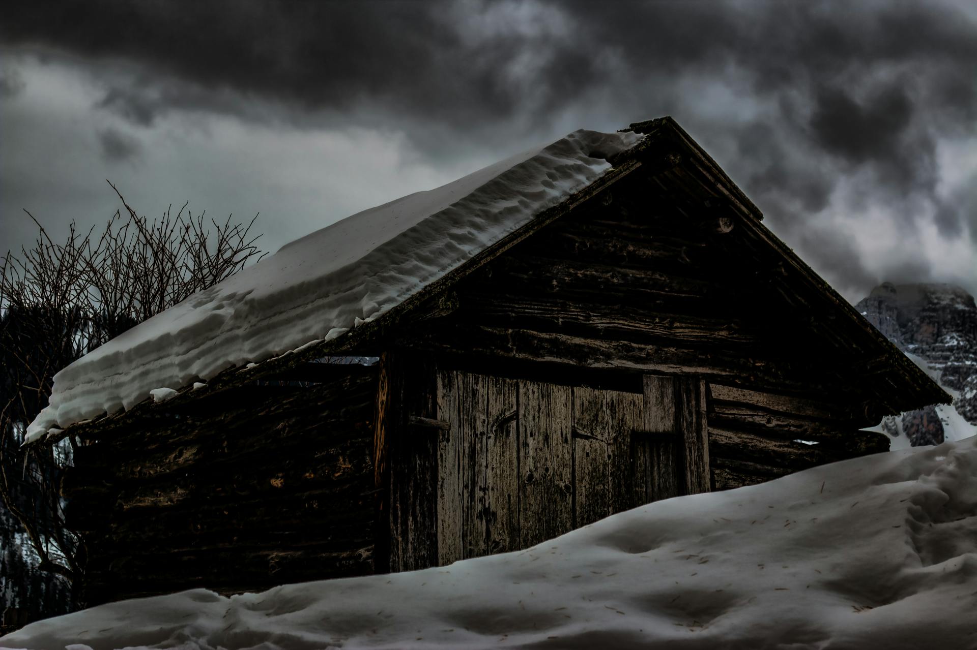 Mysterious rustic cabin blanketed in snow under a moody winter sky.