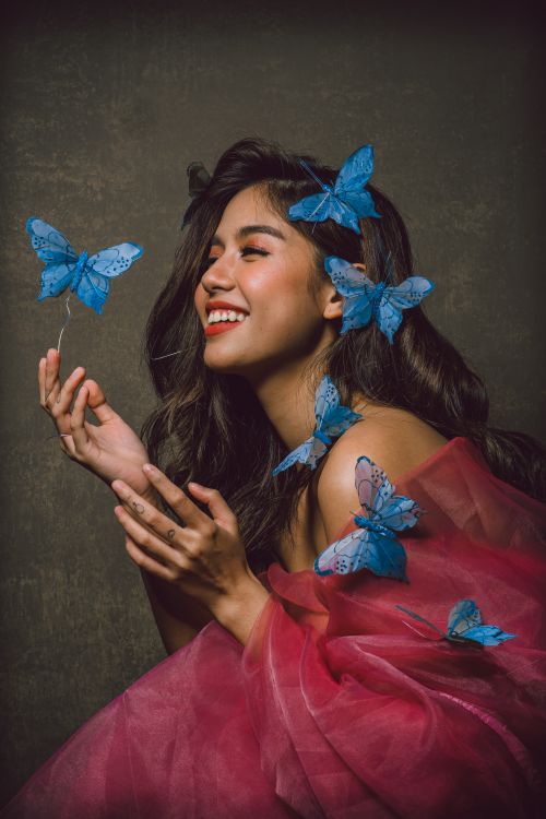 Free A woman in a red dress elegantly poses with blue butterflies, exuding joy and beauty. Stock Photo