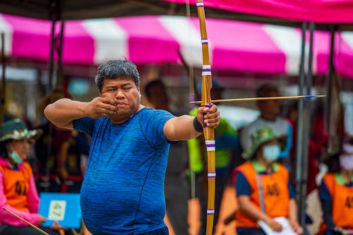 Man in Blue Crew Neck T-shirt Holding a Bow and Arrow