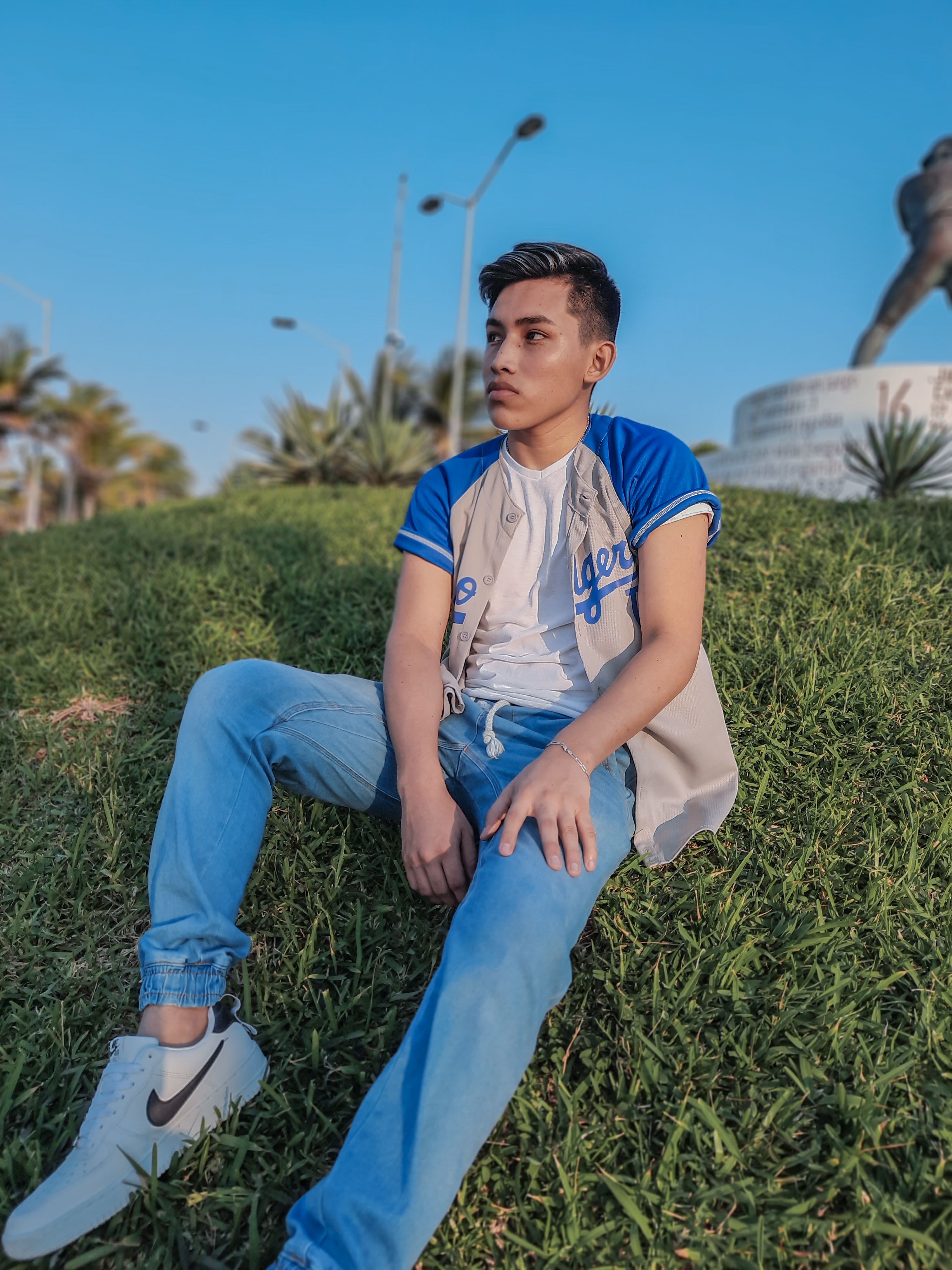 Young man in denim jeans sitting on grass, looking away in a casual style.