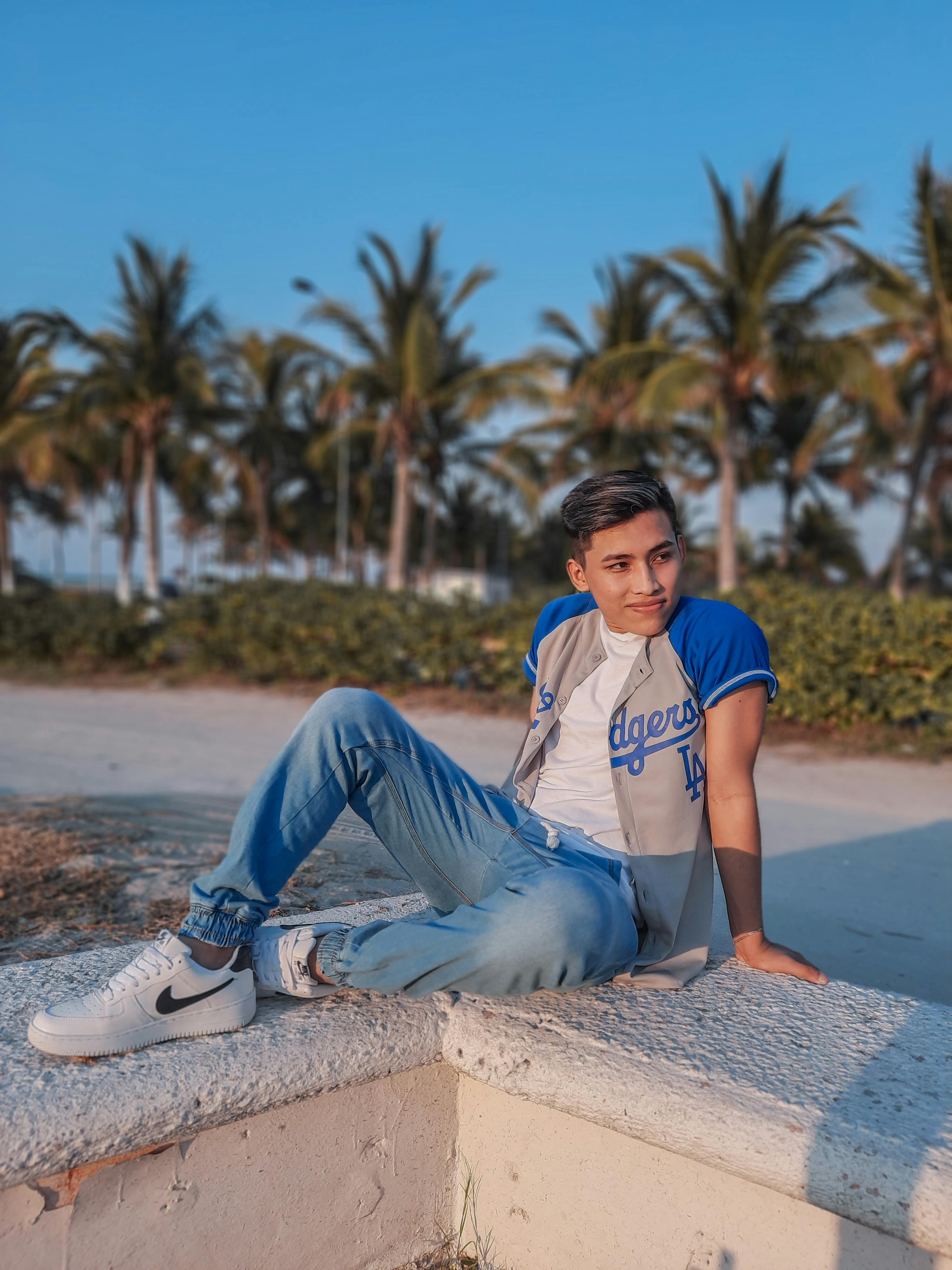 Casual portrait of a young man posing by the beach with palm trees under a clear blue sky.