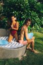2 Women in Bikini Sitting on White and Blue Striped Hammock