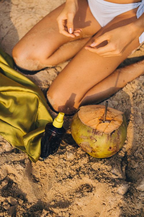 Free Kneeling woman on sandy beach with coconut and sunblock spray. Perfect summer scene. Stock Photo