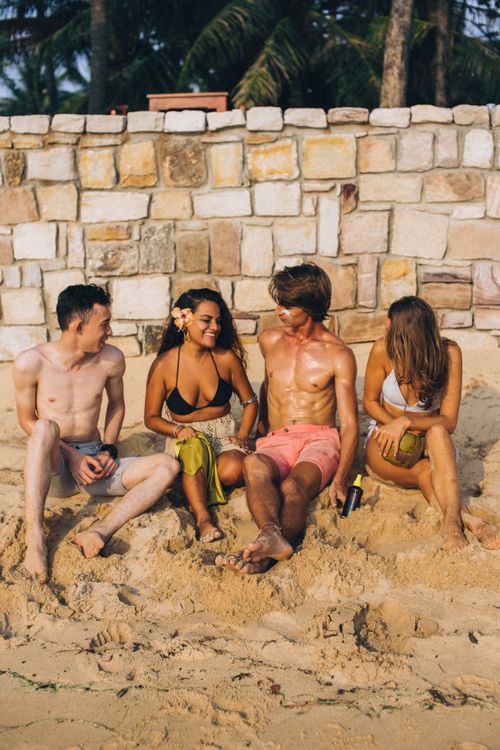 Free Four young friends sitting on a sandy beach chatting and laughing in the sun. Stock Photo