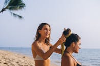 两个穿着泳装的女人在阳光明媚的海滩上扎头发，享受夏日