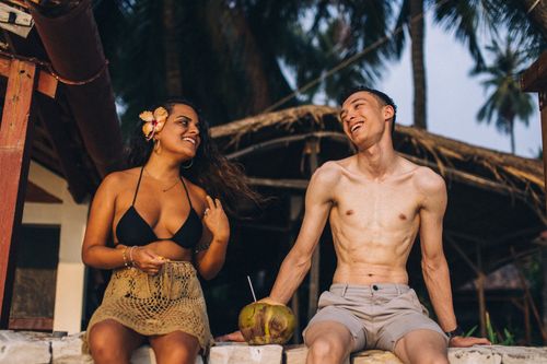 Free Happy friends chatting at a tropical resort, enjoying leisure time with a coconut drink. Stock Photo