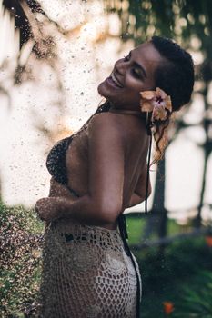 Woman in bikini with a flower in her hair, smiling under an outdoor shower.