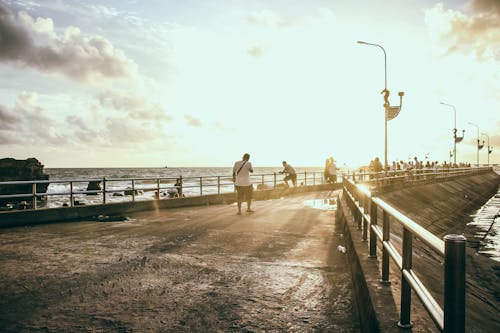 бесплатная Человек в белой рубашке, идущий по бетонному тротуару у моря Стоковое фото