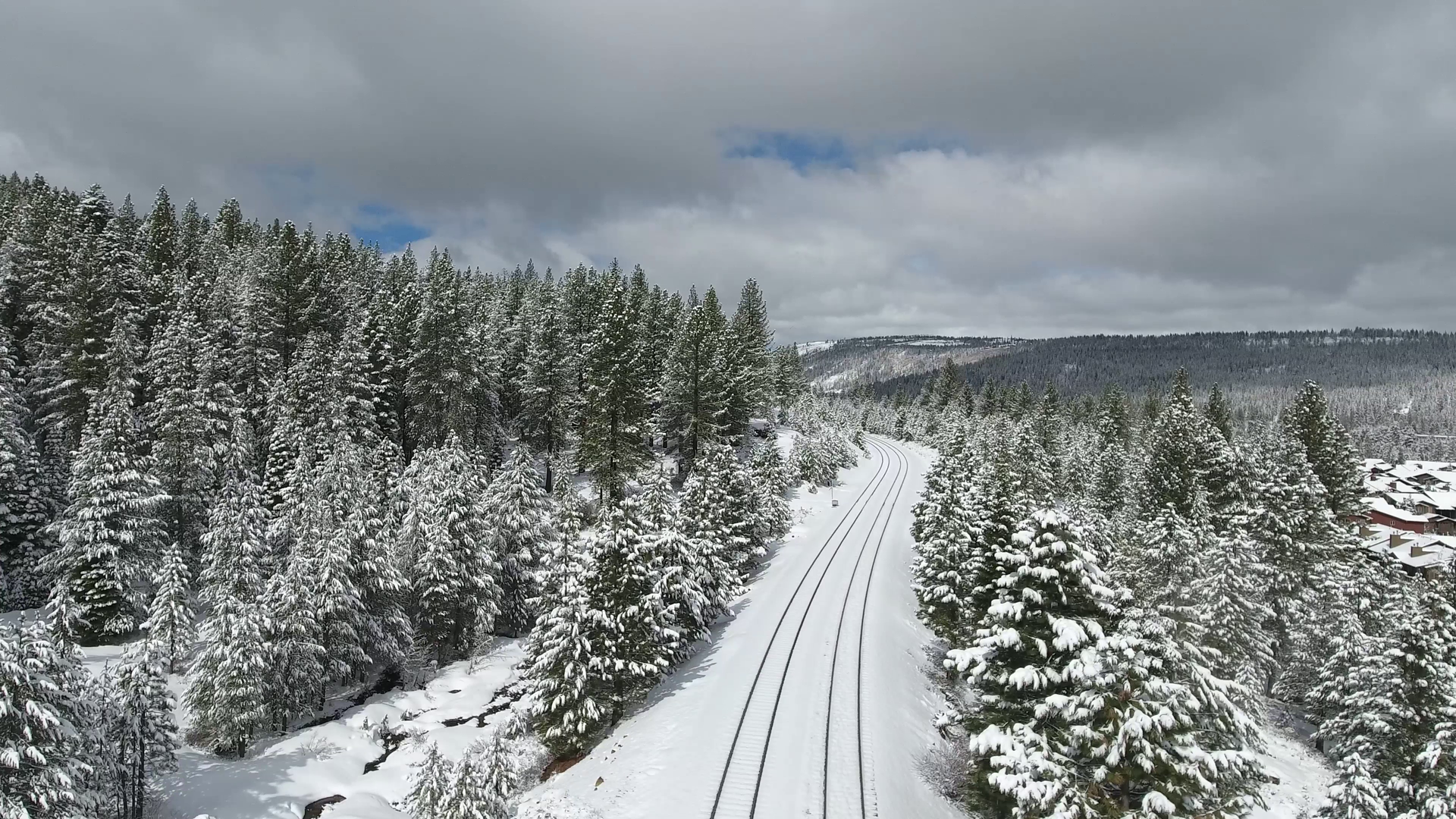 Scenic winter landscape of a railroad track winding through a snowy pine forest under cloudy skies.