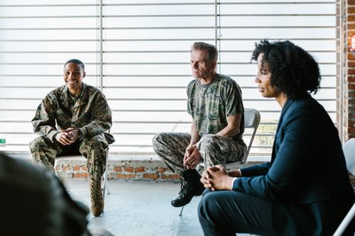 Free Military veterans engage in a supportive group therapy session with a mental health professional. Stock Photo