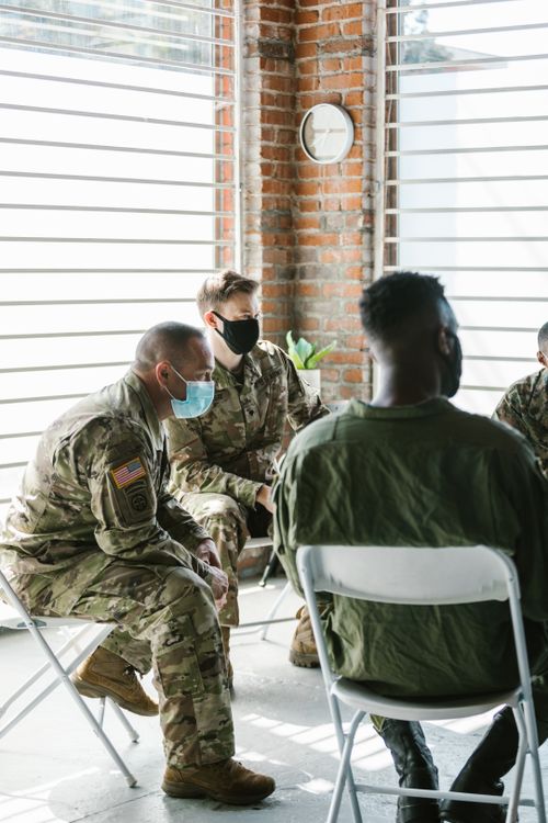 Free Military personnel engage in a healing group therapy session indoors, wearing protective facemasks. Stock Photo
