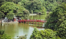 一座红桥横跨平静的河流，坐落在郁郁葱葱的森林中，风景优美，吸引人们前来探索