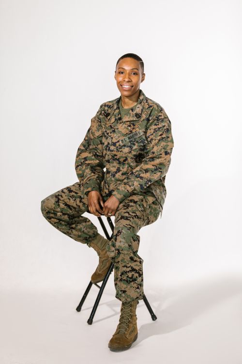 Free Smiling female soldier in camouflage uniform sitting on stool with white background. Stock Photo