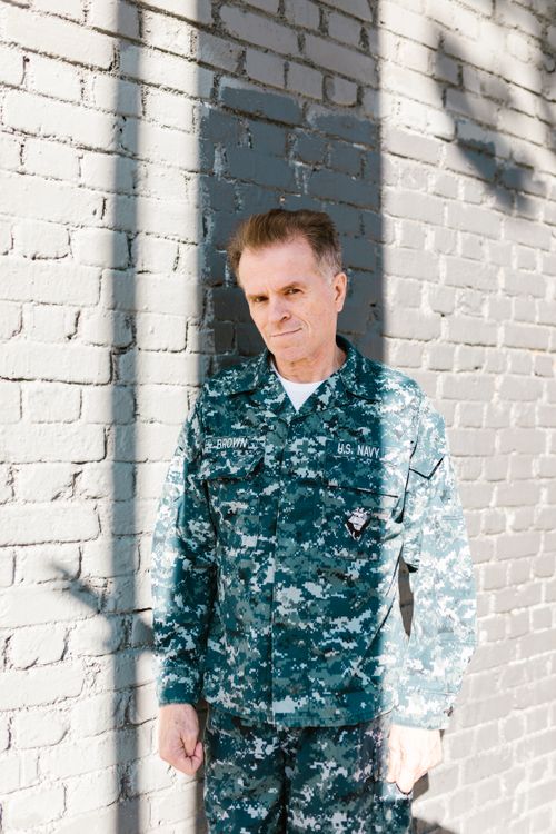 Free Senior U.S. Navy veteran standing against a brick wall in full military uniform, reflecting pride and honor. Stock Photo