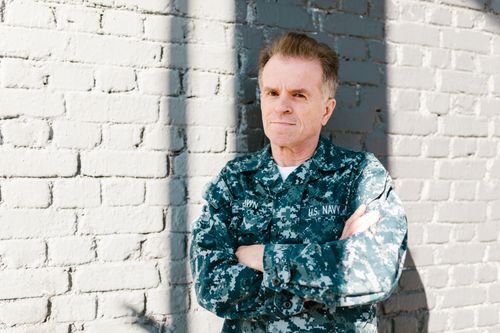 Free Senior Navy veteran standing proudly in naval uniform against a brick wall, outdoors in daylight. Stock Photo