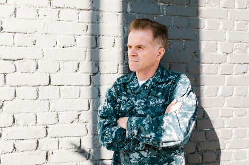 Free Senior US Navy veteran in uniform leaning against a sunlit brick wall. Stock Photo