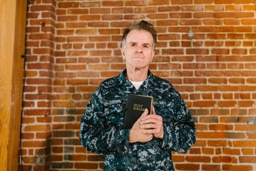 Free A senior U.S. Navy veteran holding a Holy Bible against a brick wall background. Stock Photo