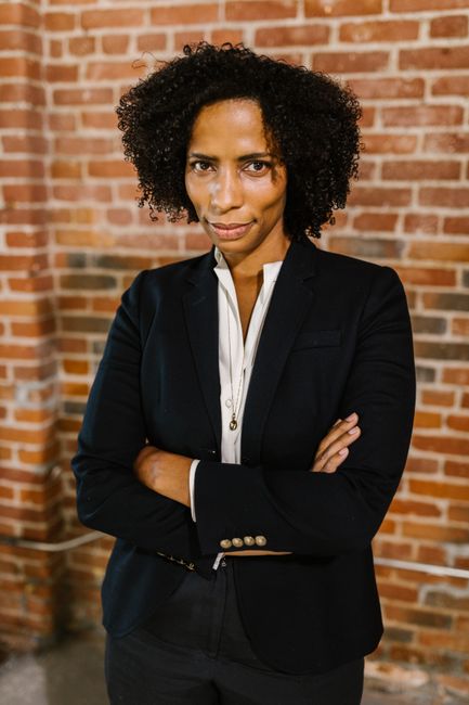 Portrait of a confident woman in a blazer against a brick wall, exuding leadership.