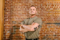 Man in Brown Crew Neck T-shirt and Brown Cargo Pants Standing Beside Brown Brick Wall