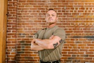 Man in Brown Crew Neck T-shirt and Brown Cargo Pants Standing Beside Brown Brick Wall