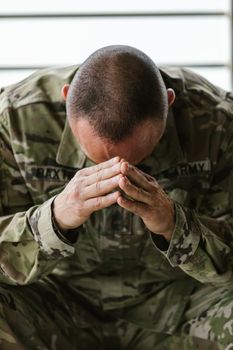 A soldier in camouflage uniform sitting with head in hands, reflecting stress and mental strain.