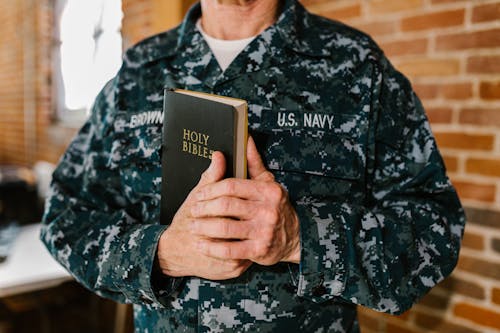 Photo of Man in Military Uniform Holding Holy Bible