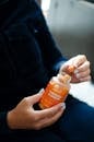 Person Holding Orange Plastic Bottle