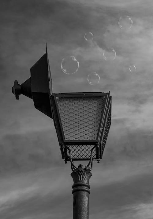 Grayscale Photo of Soap Bubbles in Air over a Lamp Post