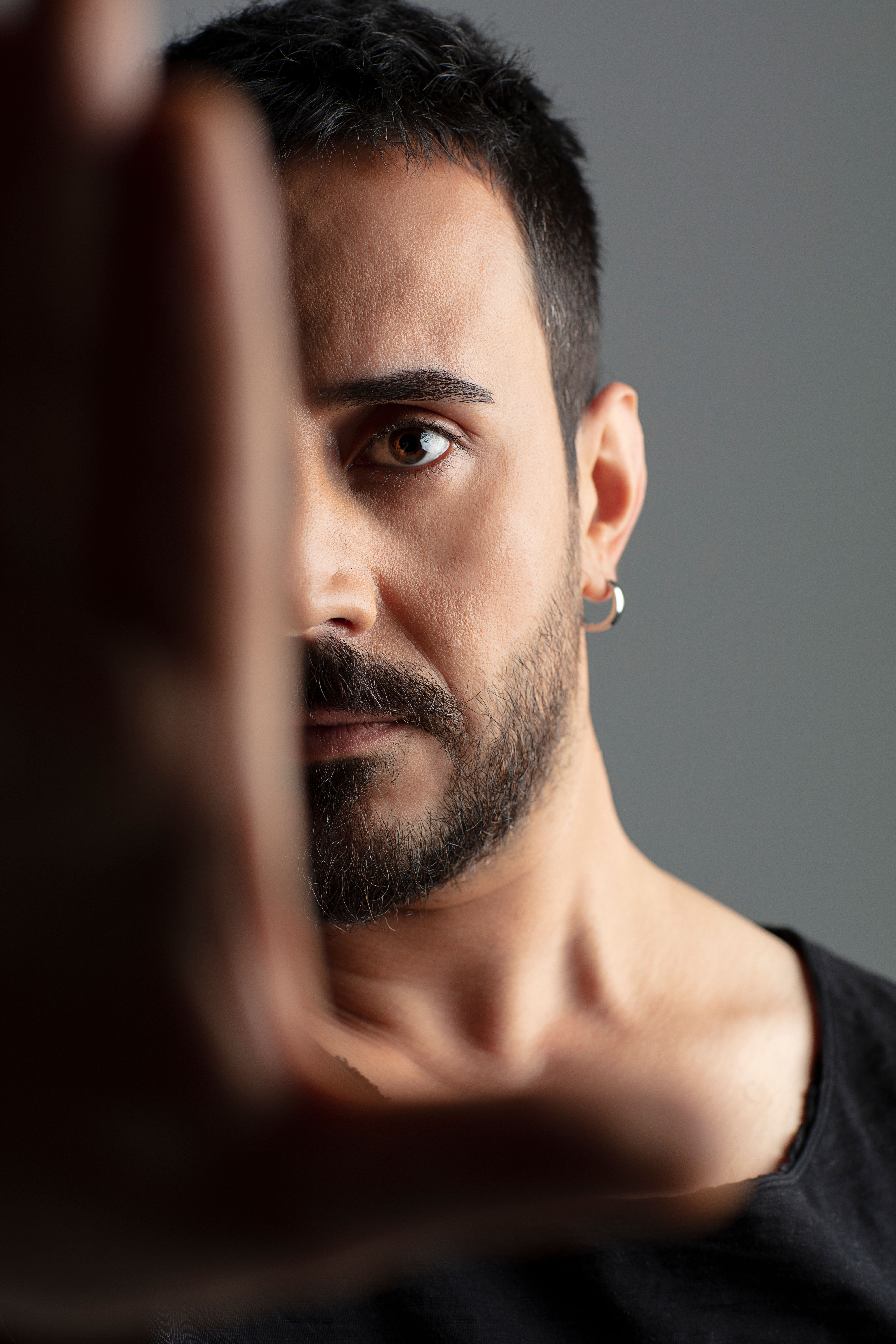Close-up of a bearded man with an intense gaze, earring visible, against a neutral background.