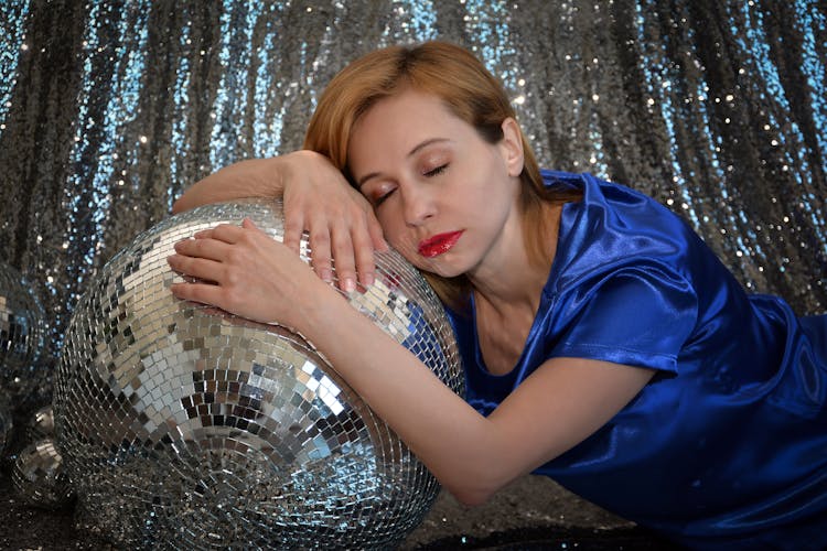 Attractive Woman Resting On Silver Disco Ball In Studio