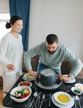 A couple setting a table with Middle Eastern cuisine during a cozy indoor gathering.