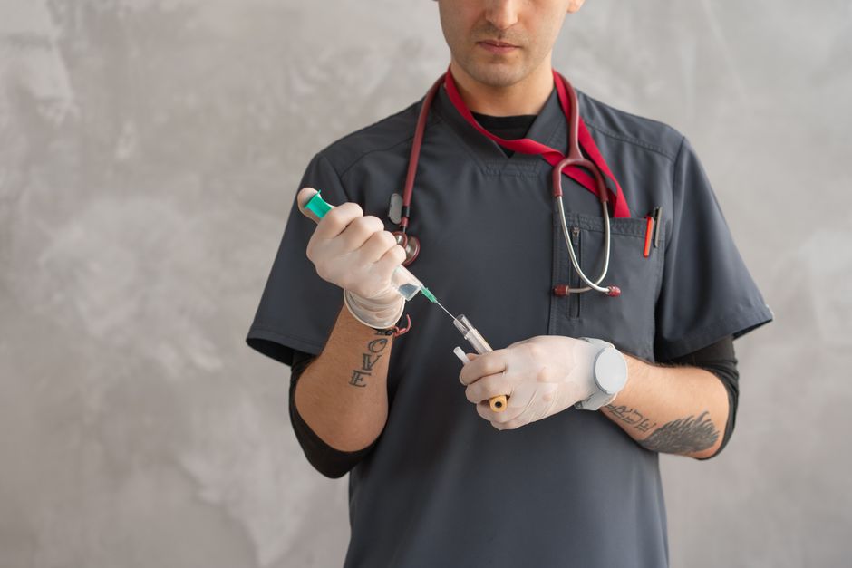 A healthcare worker in scrubs prepares a syringe with precision.