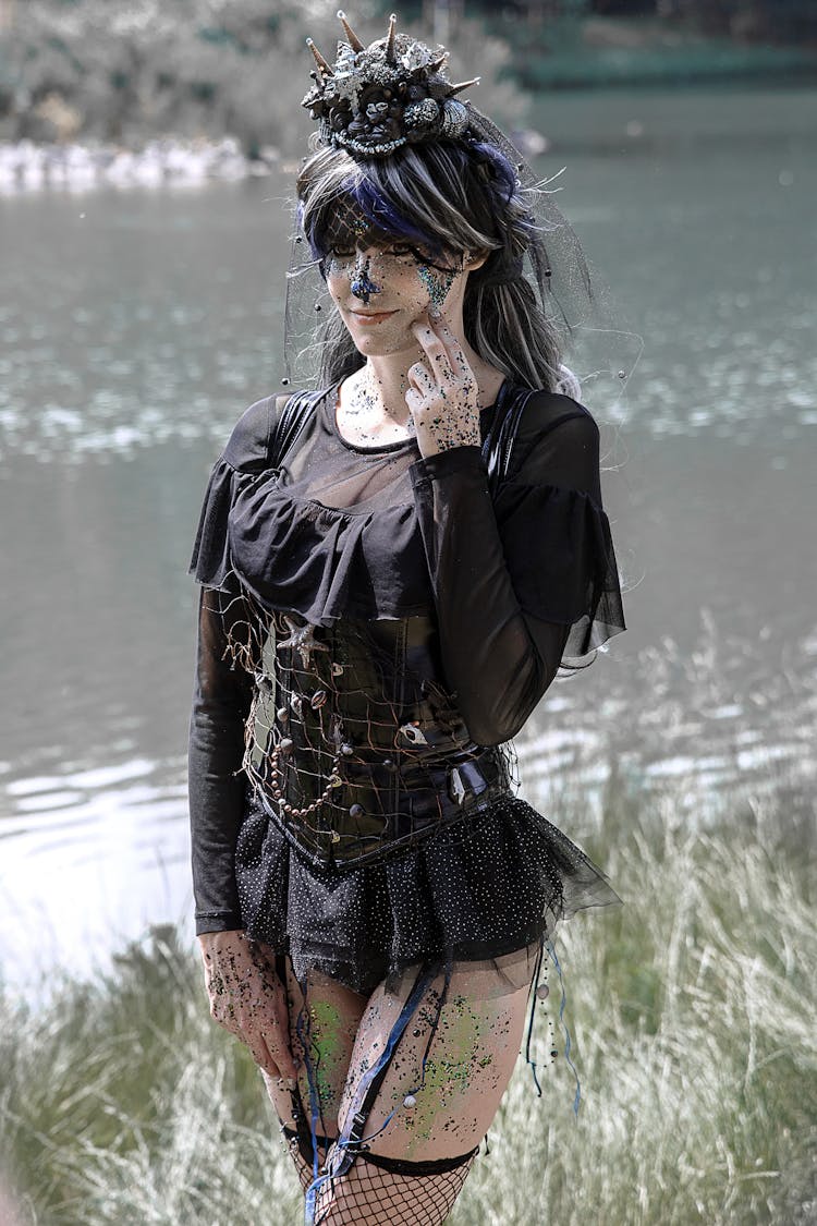 Young Woman In A Goth Black Costume And Fishnets Standing By A Body Of Water 