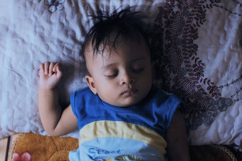 Little ethnic kid sleeping on comfortable bed at home