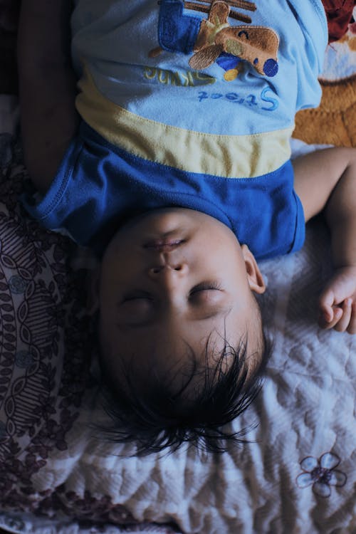 Free From above of calm little ethnic kid in pajama lying on comfortable blanket on bed in bedroom at home Stock Photo