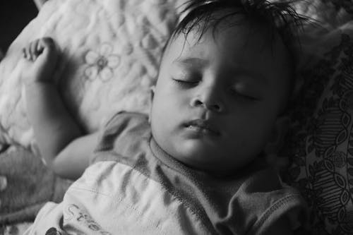 Free Black and white of calm ethnic kid in pajama lying with closed eyes on comfortable bed in bedroom at home in daytime Stock Photo