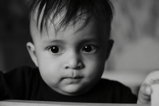 A close-up black-and-white portrait capturing the curious expression of a toddler indoors.
