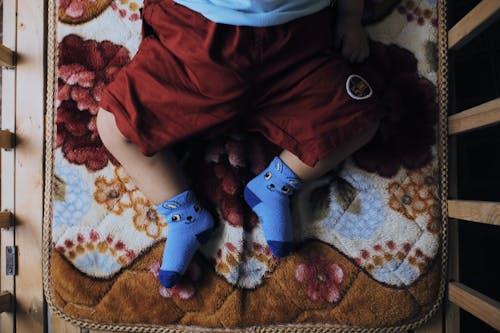 Free From above crop view of little adorable feet of kid in red shorts and blue socks with print lying on cozy plaid in baby cot in daylight Stock Photo