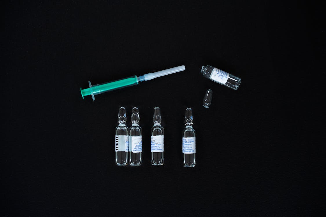 Free A close-up view of glass ampoules and a syringe on a black background, representing medical supplies. Stock Photo