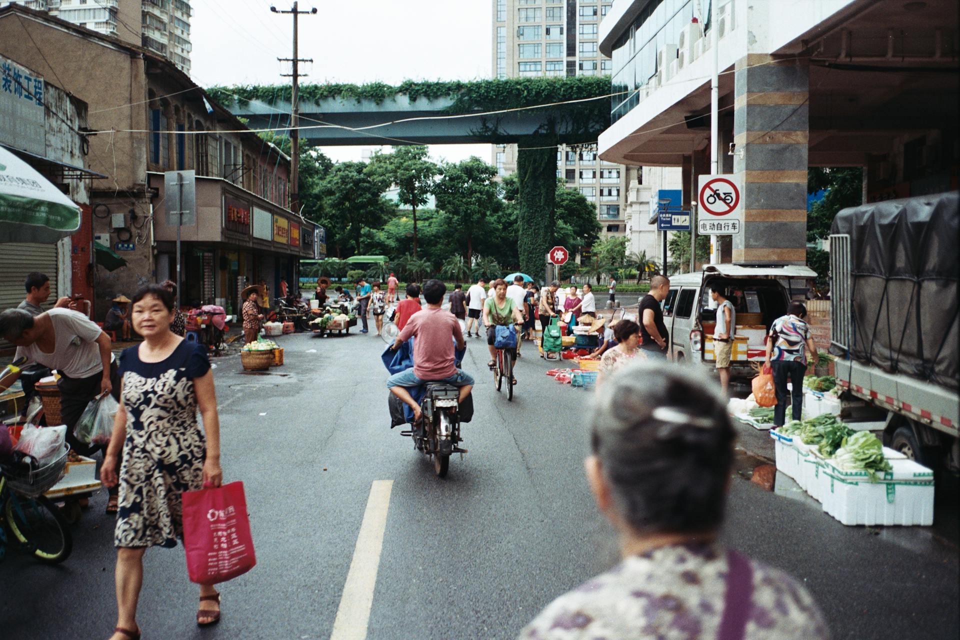 Street market scene in Xiamen, China with people shopping, cycling and stalls lining the street.