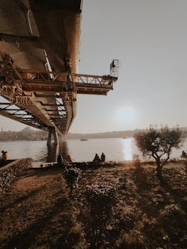 Capture of a bridge over a river at sunrise, with people on the riverbank enjoying the view.