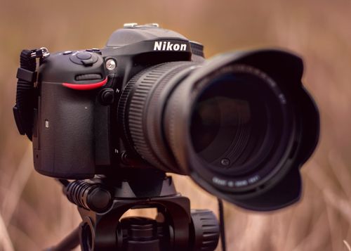 Free A close-up view of a Nikon DSLR camera mounted on a tripod, set against an outdoor backdrop. Stock Photo