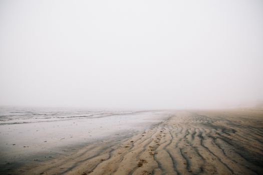 Serene foggy beach scene with ripples in the sand and calm sea.