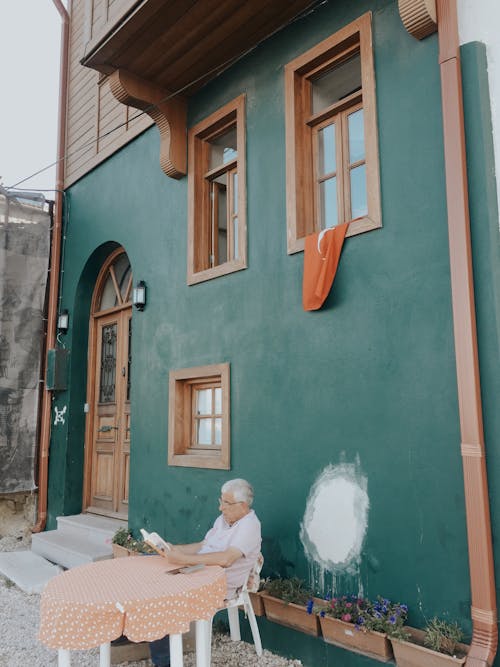 Photo of an Elderly Man Sitting in Front of a House